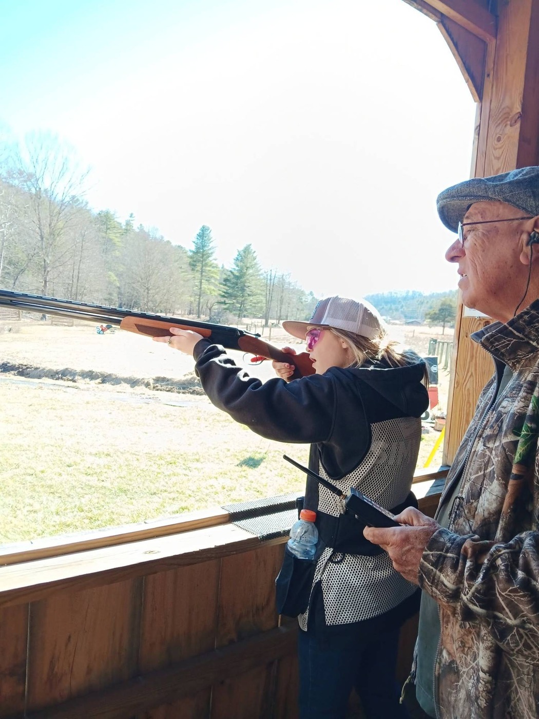 A young shooter in pink safety glasses taking aim, with an older man beside her