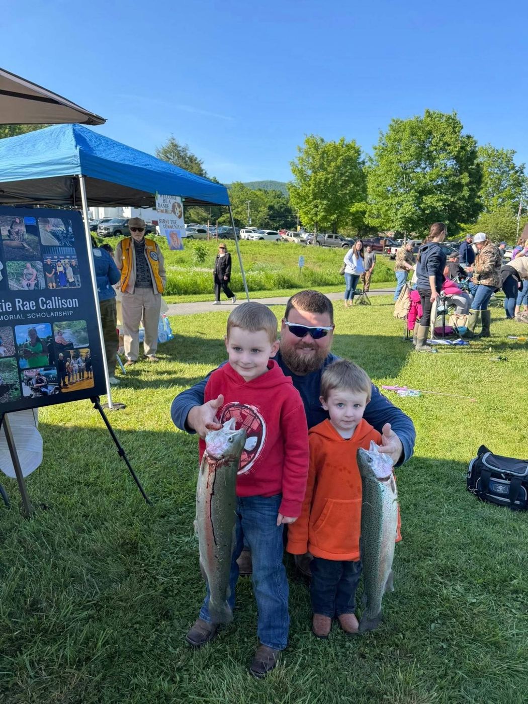 A man and two young boys each holding a large trout at the Fishing Derby
