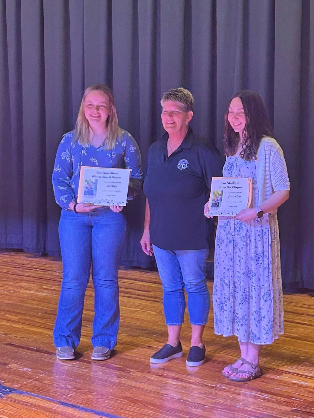 Two scholarship recipients holding their certificates on stage with a GVSA member