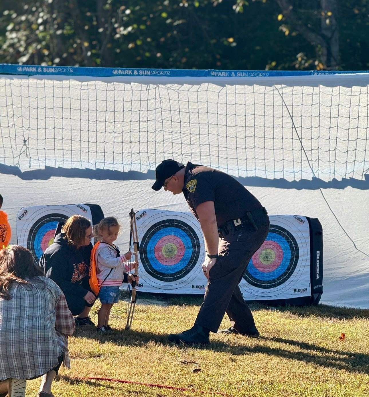 A police officer helping a young child hold a bow at the archery station at Youth Day 2025