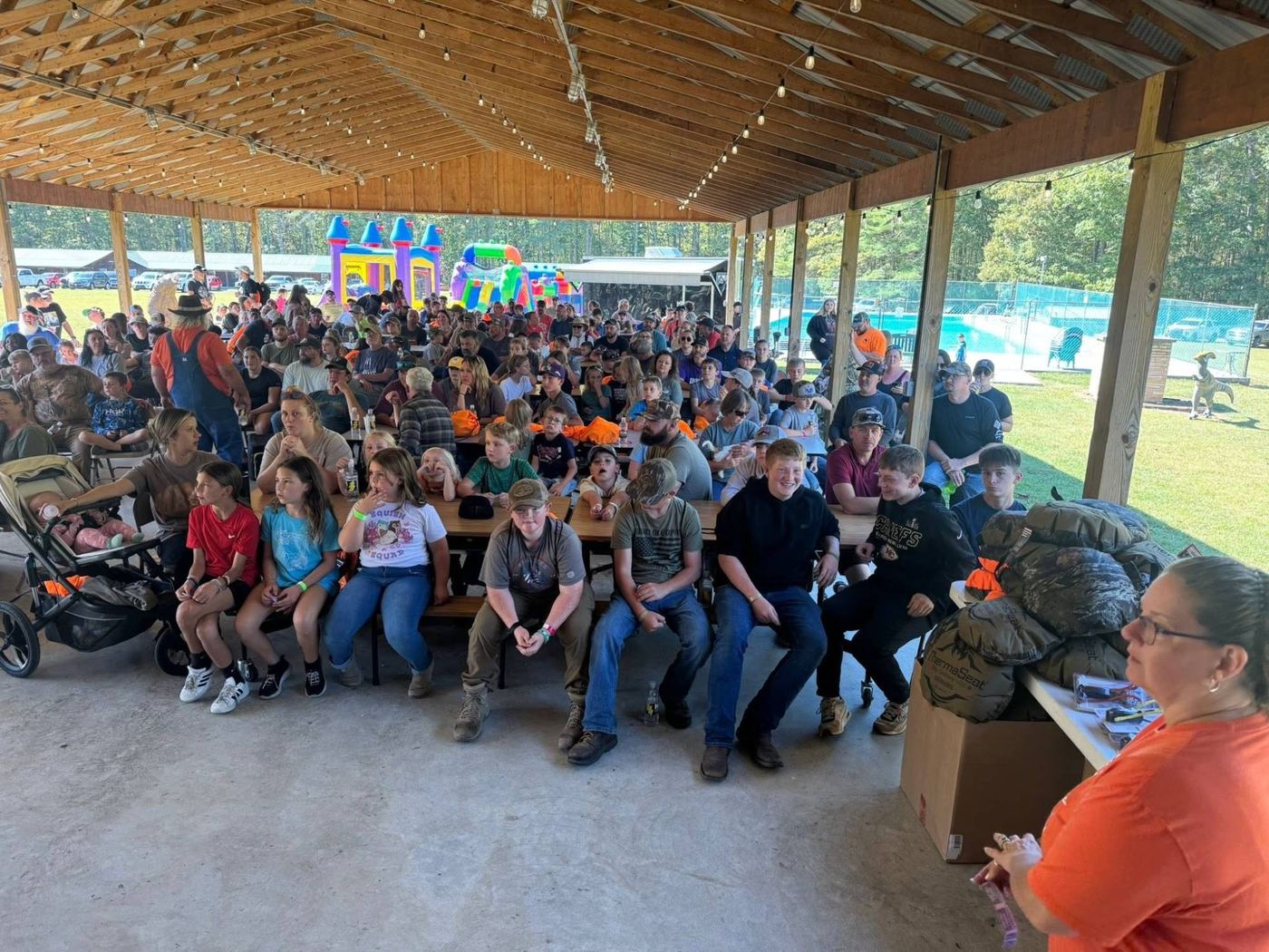 A crowd of kids and families seated at picnic tables under a pavilion at Youth Day 2025